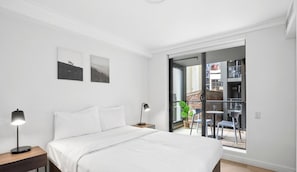 Una camera da letto con un letto, abat-jour e vista su un balcone esterno con sedie e una pianta.