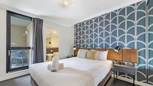 Ein Hotelzimmer mit Bett, Nachttisch, Lampe und Blick auf einen Balkon.