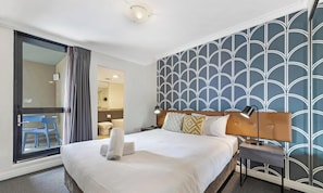 A hotel room with a bed, bedside table, lamp, and a view of a balcony. - KozyGuru | Haymarket | High Level 2B APT 16 (Haymarket)