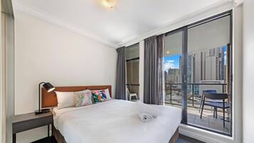 A hotel room with a large bed, a nightstand, a desk, a chair, and a balcony with a city view.