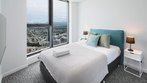 A hotel room with a large window, a bed with a teal headboard, two bedside lamps, and a neatly made bed.