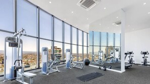 A modern gym with large windows offering a city view, equipped with various exercise machines and weights.