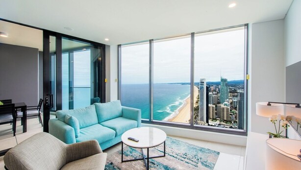 A modern living room with a large window, a sofa, a coffee table, and a view of the ocean and city skyline.