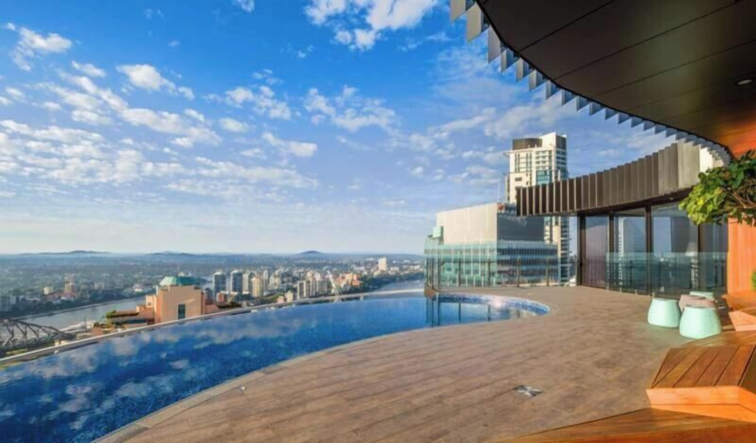 A rooftop infinity pool with a city view, modern architecture, and a wooden deck.
