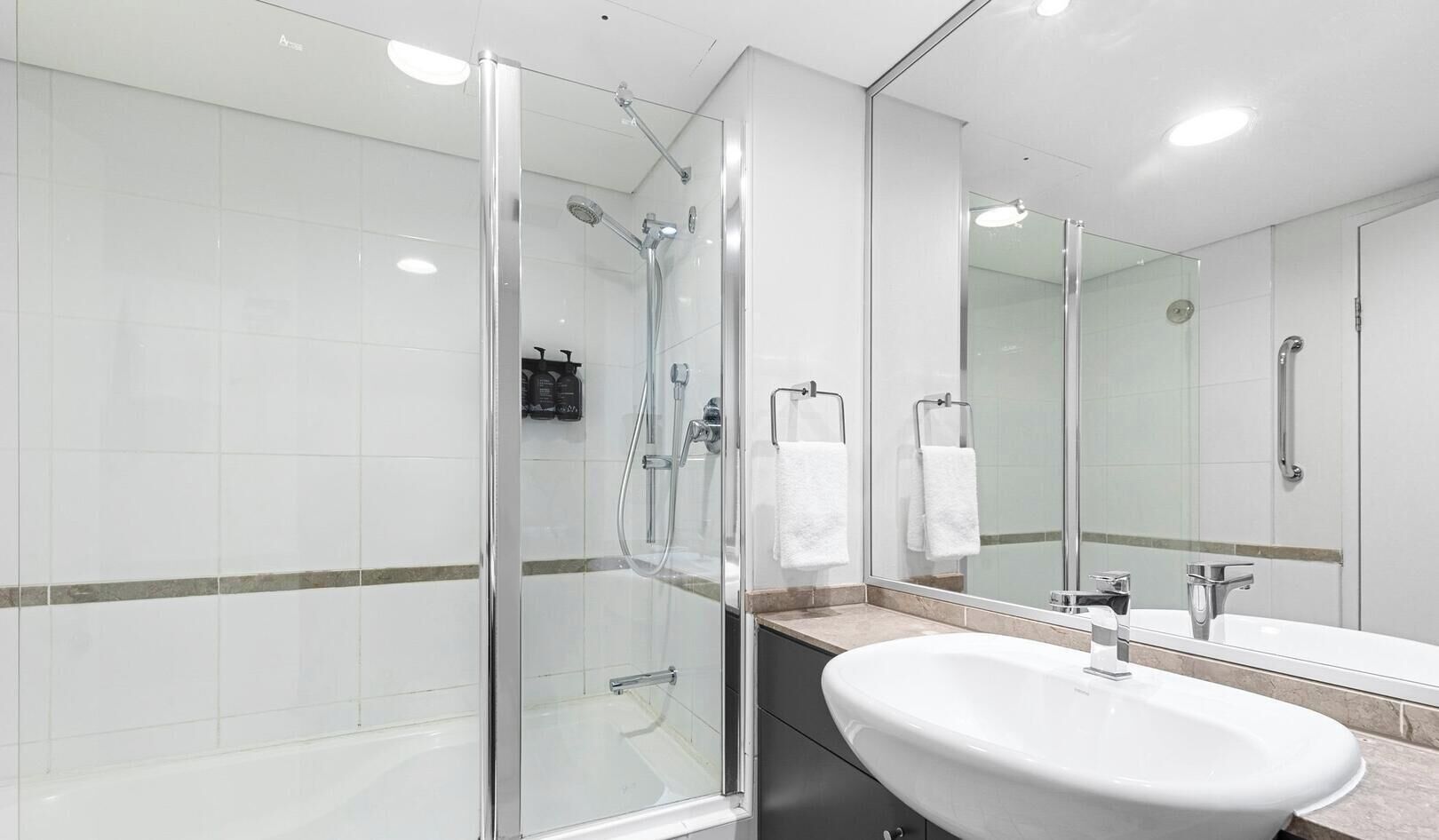 Une salle de bain moderne avec une douche à parois de verre, un grand lavabo et un miroir.