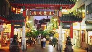 Una puerta tradicional china con un letrero, rodeada de tiendas y gente caminando.