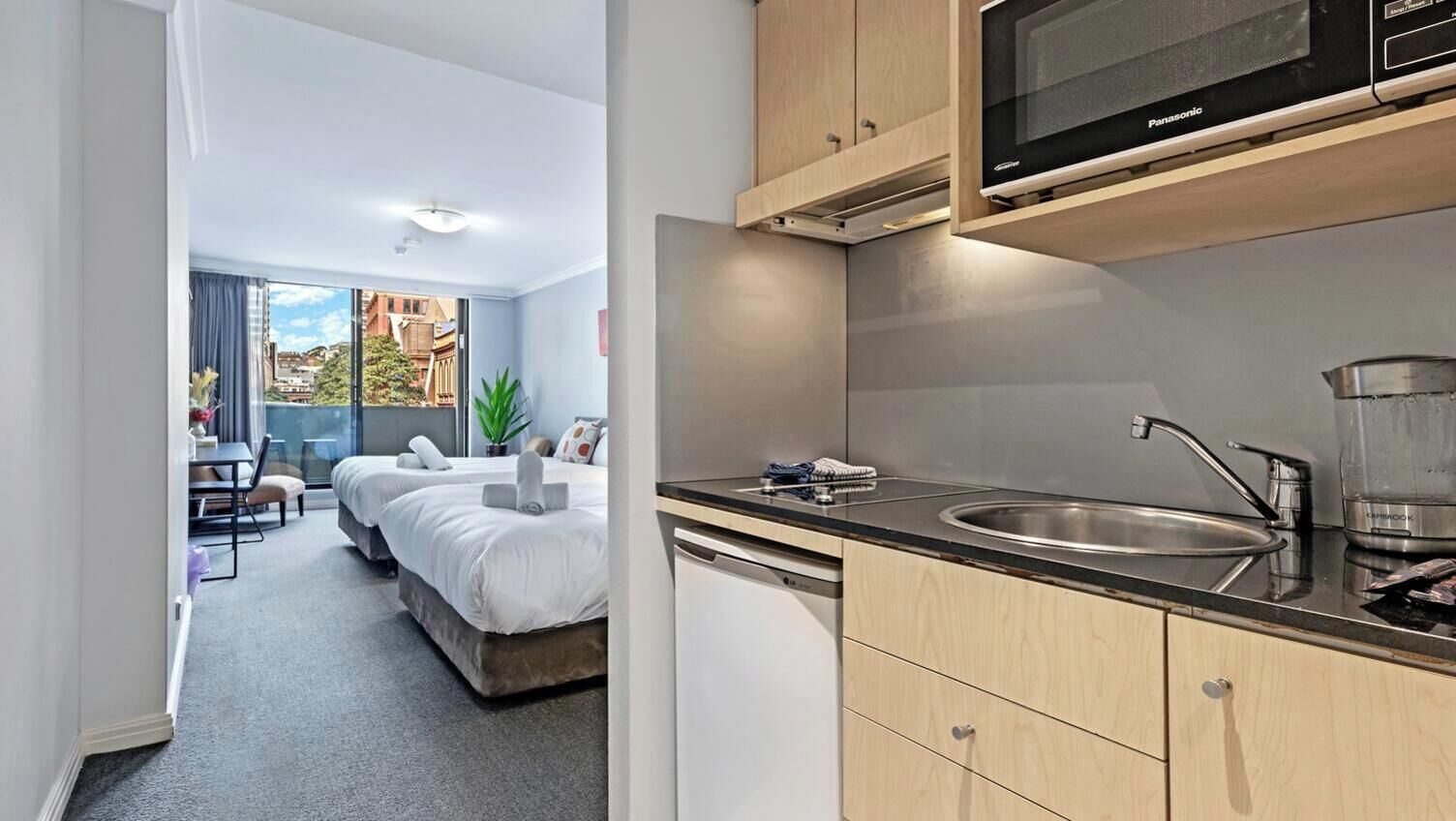 A hotel room with a kitchenette, a bed, a dining area, and a view of the outside.
