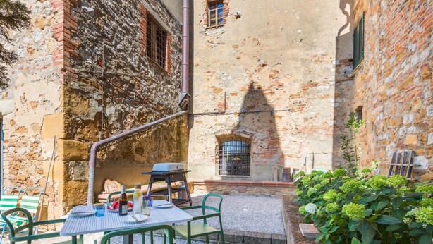 Un patio con mesa y sillas, una parrilla y una pequeña zona ajardinada.