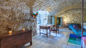 Una habitación rústica con paredes de piedra, un escritorio de madera, sillas y una hamaca colorida.