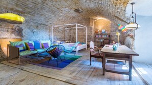 Una habitación acogedora con pared de piedra, una cama con ropa de cama colorida, una mesa de madera, una silla y una estantería.