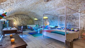Una habitación acogedora y rústica con pared de piedra, suelo de madera, cama con dosel, una pequeña mesa con velas y sillas coloridas.