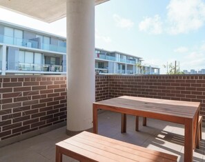 Une terrasse sur le toit avec une table et un banc en bois, des murs en briques et une vue sur un immeuble moderne.