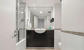 A modern bathroom with a glass shower enclosure, a white sink, dark cabinets, and a white toilet.