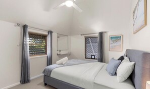 A bedroom with a bed, a ceiling fan, a window with curtains, a bedside table, and a framed picture on the wall.