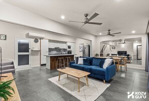 Uma sala de estar moderna com um sofá azul, mesa de centro de madeira e uma área de cozinha com balcão.