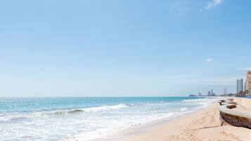 A beach with a clear sky, a sandy shore, and a row of buildings along the coastline.