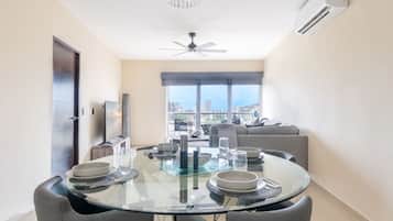 A modern dining area with a glass table, chairs, and a city view through large windows.