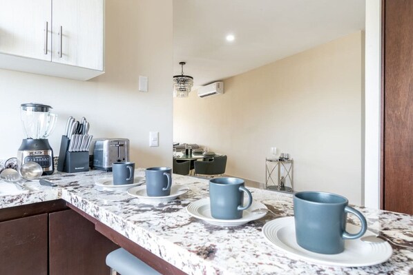 Una cocina con encimera de mármol, cafetera, tostadora y candelabro.