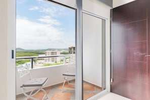 A balcony with a view of buildings and greenery, a sliding glass door, and two white chairs.