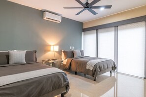 Una habitación de hotel moderna con dos camas, un ventilador de techo, un equipo de aire acondicionado y un ventanal con persianas.