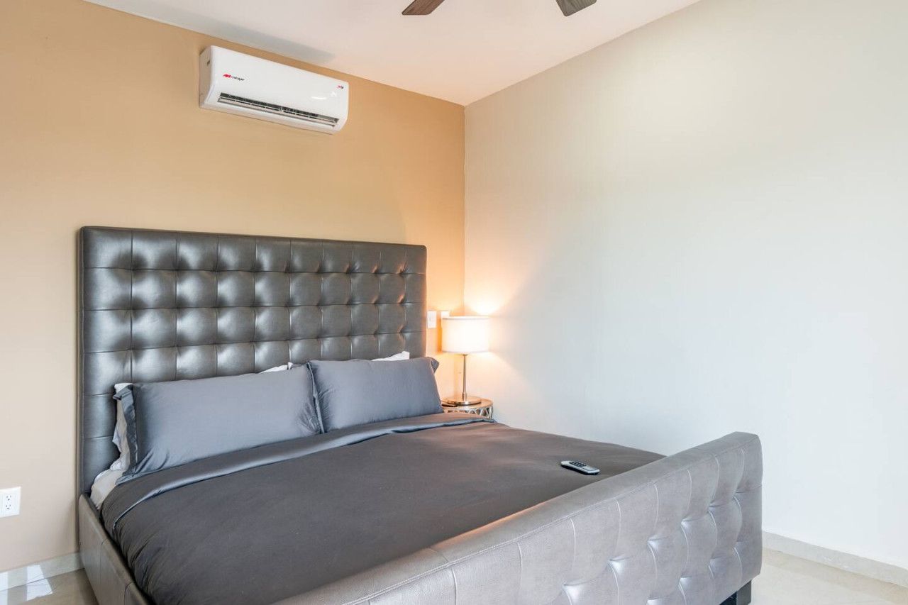 A hotel room with a large bed, a bedside lamp, and an air conditioning unit on the wall.