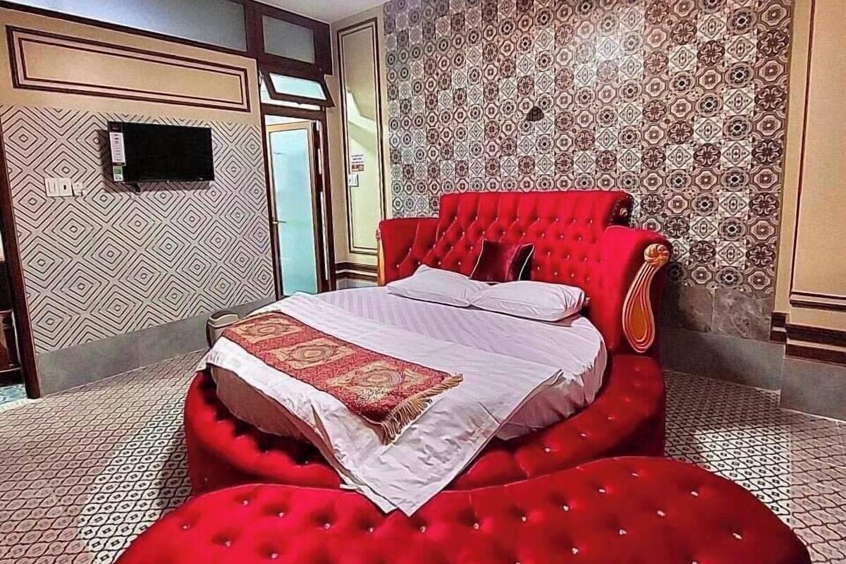 Quarto com cama grande, um banquinho vermelho, televisão e papel de parede estampado.