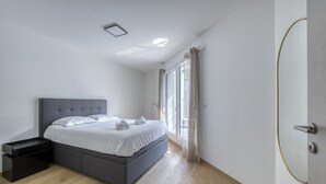 A modern bedroom with a large bed, a nightstand, and a sliding door leading to a balcony.