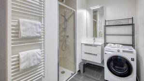 A modern bathroom with a glass-enclosed shower, a white sink, a mirror, and a front-loading washing machine.
