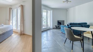 A modern, well-lit room with a bed, a sofa, a dining table, and a TV.