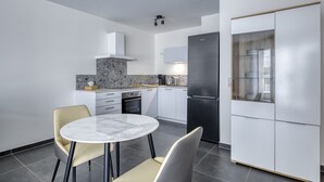 A modern kitchen with white cabinets, a black refrigerator, and a marble-top dining table with two chairs.