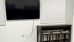 Een moderne woonkamer met een flatscreen televisie aan de muur, een houten salontafel en twee blauwe fauteuils.