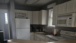 A kitchen with white cabinets, a white refrigerator, a microwave, a sink, and three wooden stools. - Charming, 1-bdrm apt, visit the Marshwalk, Huntington St Pk & Brookgreen Gardens (Murrells Inlet)