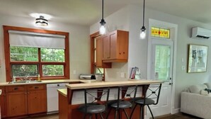 Une cuisine avec des meubles en bois, un coin bar avec des tabourets, une fenêtre donnant sur un espace verdoyant et une porte ornée d’un vitrail.