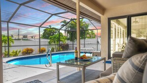 Un espace aménagé au bord de la piscine, avec une table en verre, des chaises longues et une vue sur la piscine et la végétation environnante.