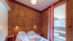 A wooden room with two beds, a small table, and a sliding door to an outdoor area. - Les Sentes by Interhome (Maubuisson)