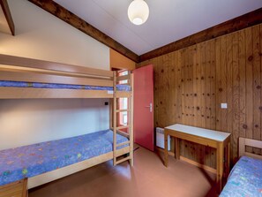 A bunk bed room with a wooden ceiling, a small table, and a red door.