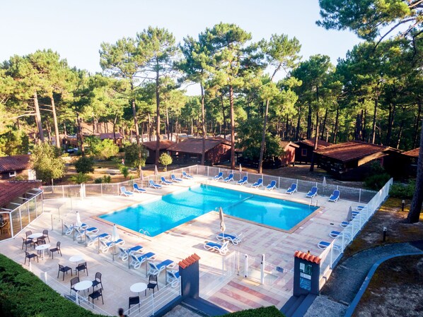 A pool area with lounge chairs and tables, surrounded by trees and buildings.