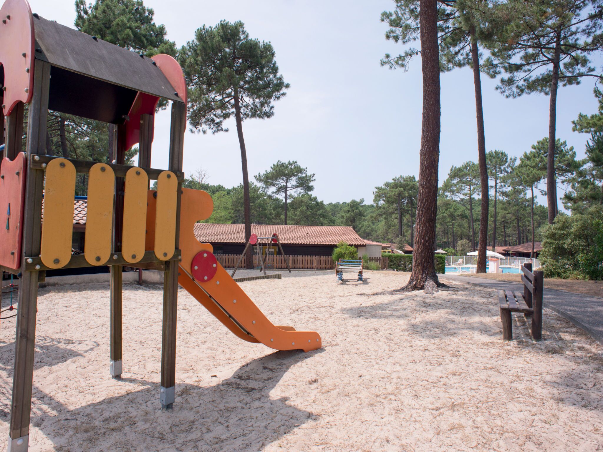 Un parque infantil con tobogán y estructuras para escalar, rodeado de árboles y una zona de arena.