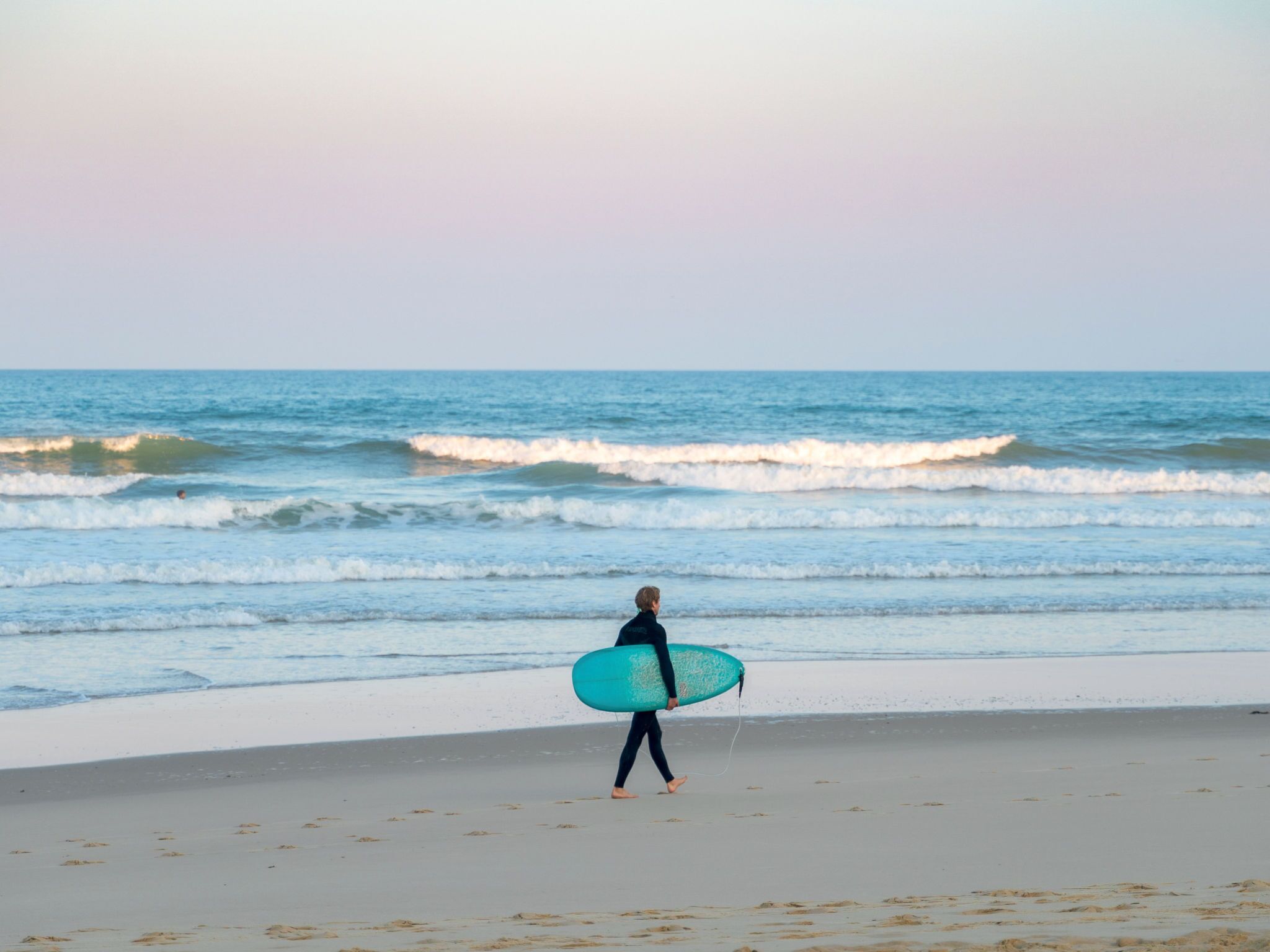 Eine Person geht am Strand mit einem Surfbrett.
