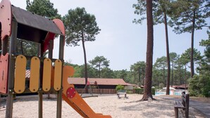 A playground with a slide and climbing structures, surrounded by trees and a sandy area. - Les Sentes by Interhome (Maubuisson)