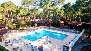 Zona de piscina amb gandules i taules, envoltada d'arbres i edificis.