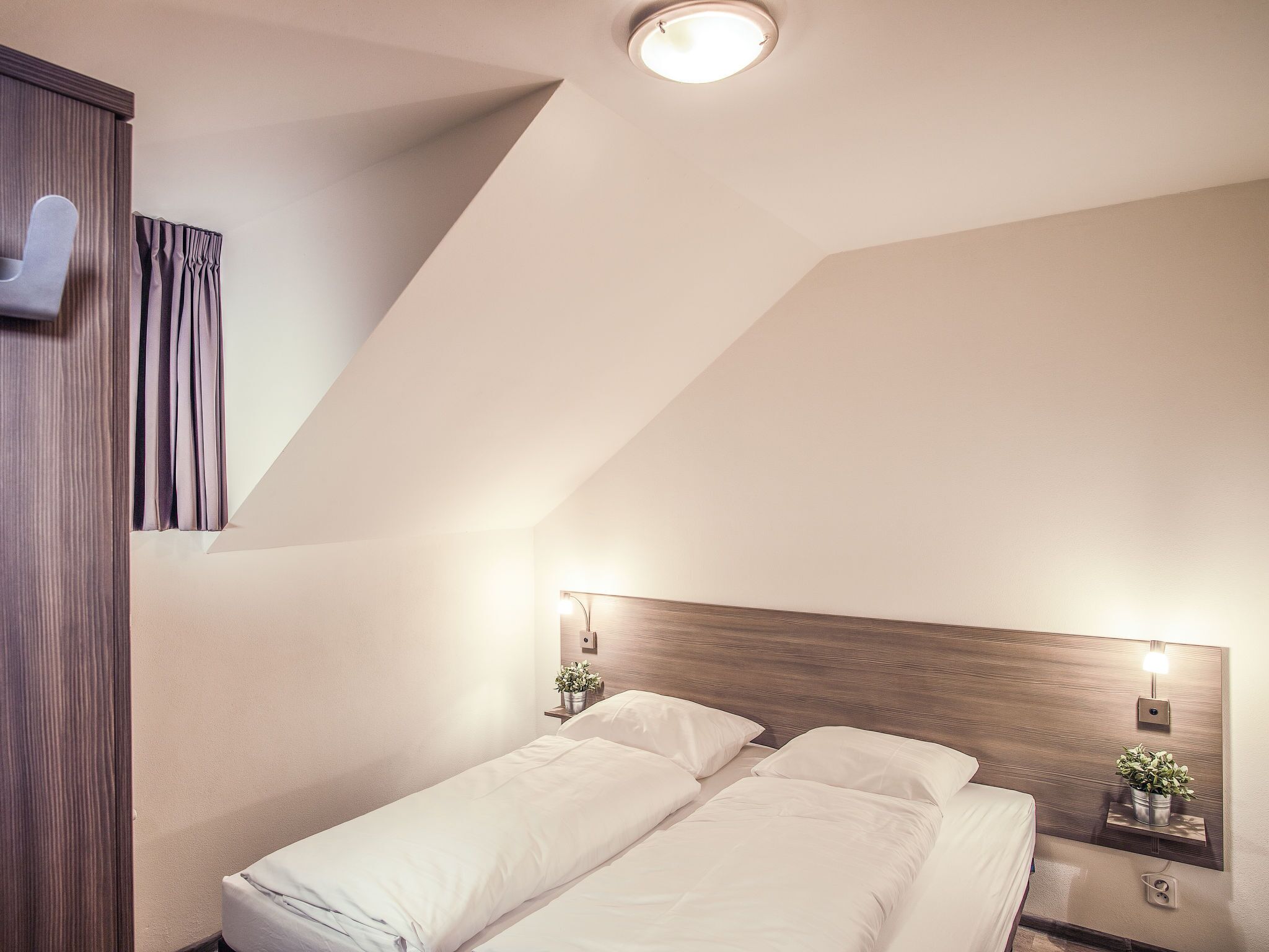 A hotel room with a single bed, a nightstand with a lamp, and a ceiling light.