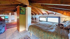 Een slaapkamer met een schuine plafond, een bed, een bureau en een televisie.