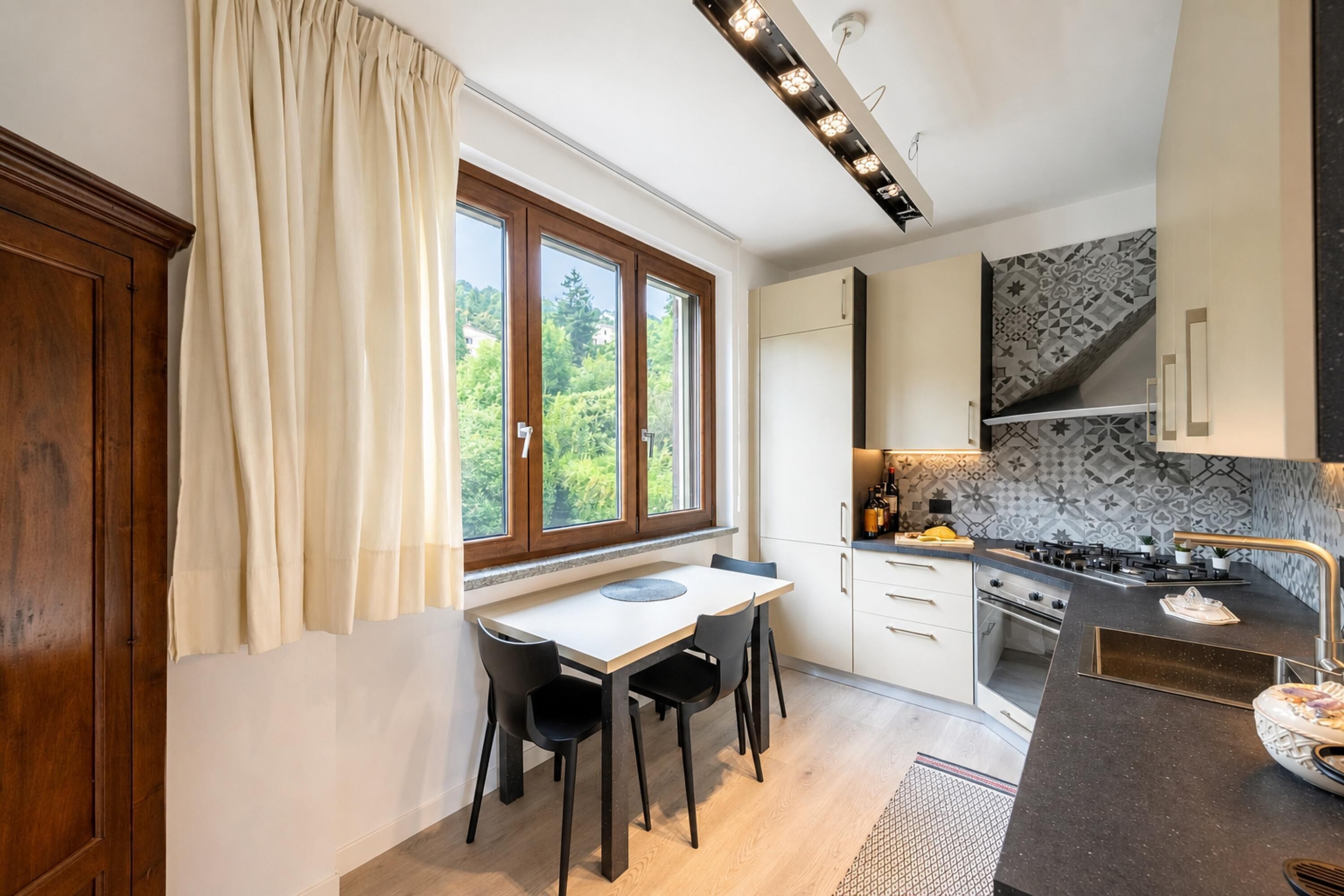 Une cuisine moderne avec un coin repas, des meubles en bois, une fenêtre avec des rideaux et un crédence décorée.