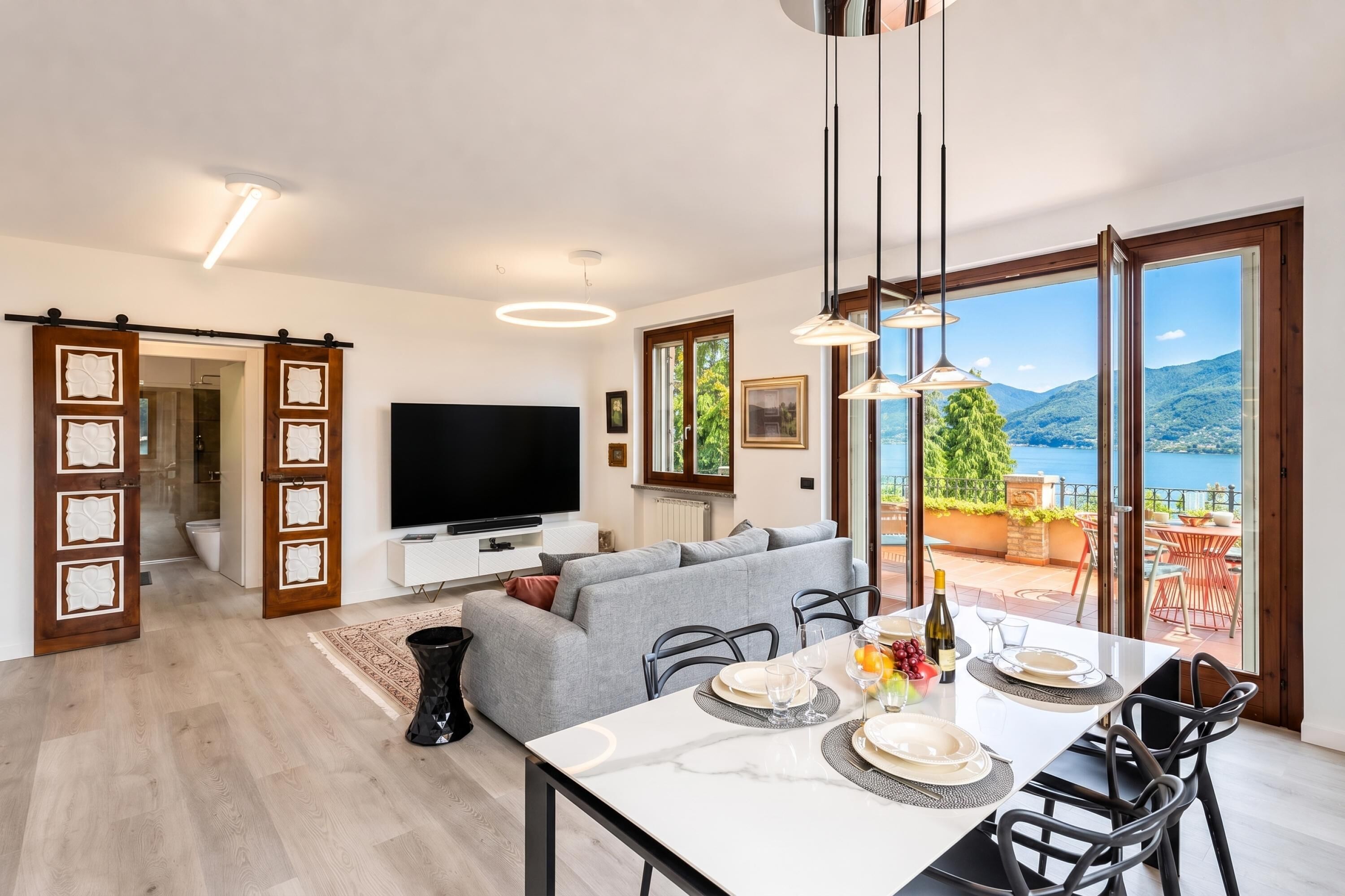 Un salon moderne doté d’un téléviseur à écran plat, d’un canapé gris, d’une table à manger pour quatre personnes et offrant une vue imprenable sur les montagnes grâce à de grandes fenêtres.