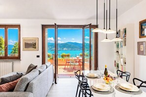 A modern living room with a sofa, dining table set for four, and a view of a mountainous landscape through large glass doors.
