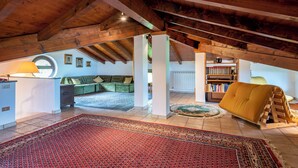 Een zolderkamer met zichtbare houten balken, een groene bank, een geel poufje en een boekenkast.