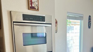 Eine Küche mit Einbauofen, einer kleinen Topfpflanze und einem Fenster mit Jalousien.