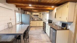 Una cocina con vigas de madera, una mesa de comedor con sillas y un armario blanco grande.