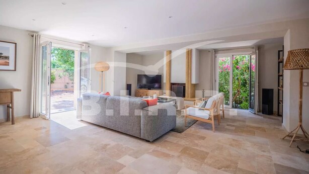 A spacious living room with a grey sofa, a wooden coffee table, and a TV. There are large sliding glass doors leading to a garden. - GASSIN BEAUTIFUL VILLA WITH SWIMMING POOL (GASSIN)